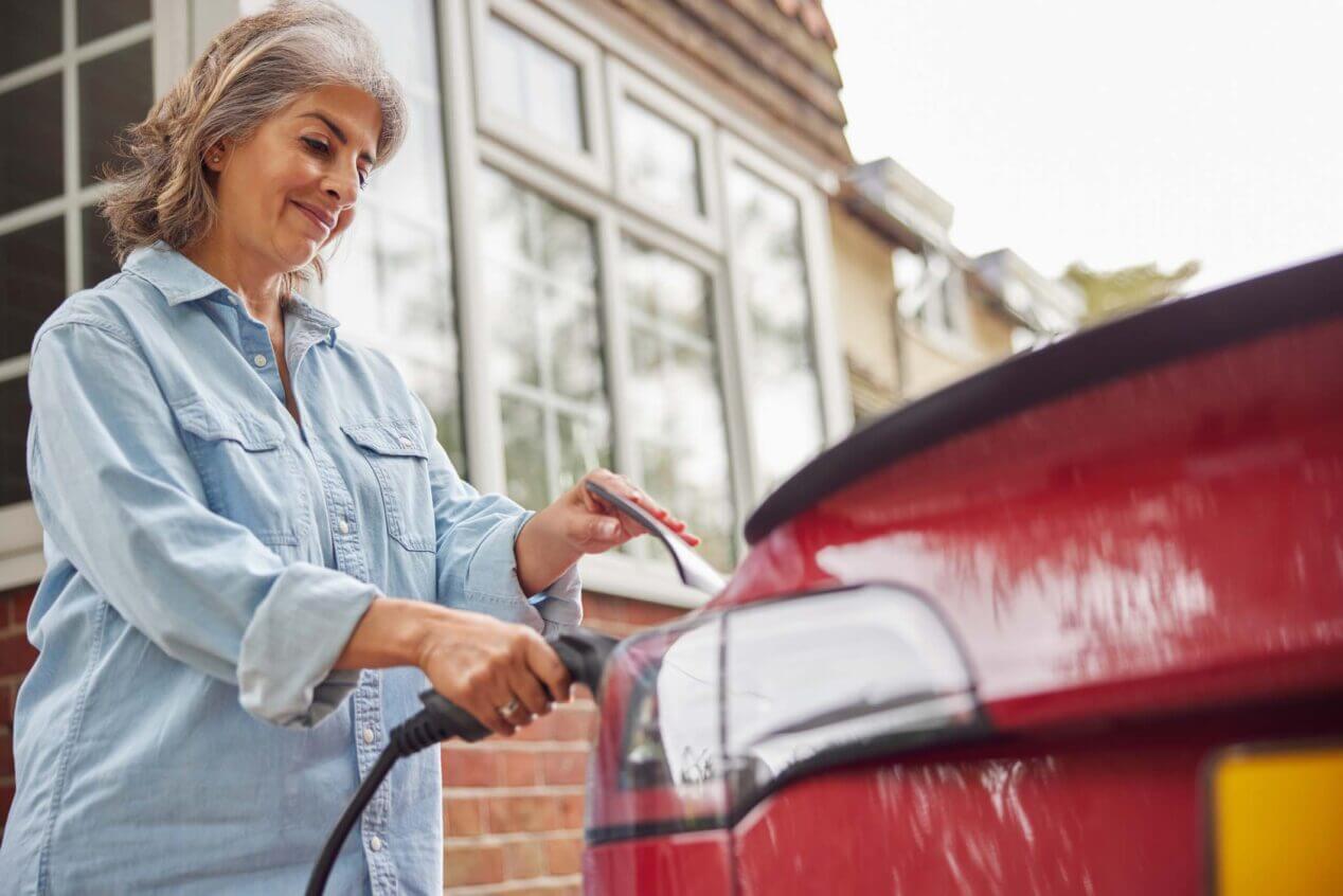 A woman smiles as she plugs in her electric vehicle