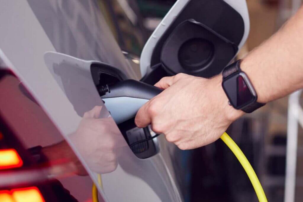 A closeup of a man with a watch as he plugs in his electric vehicle.