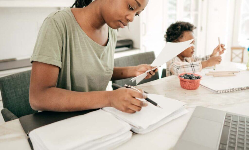 A woman sits at the counter, going through paperwork as her son plays in the background.